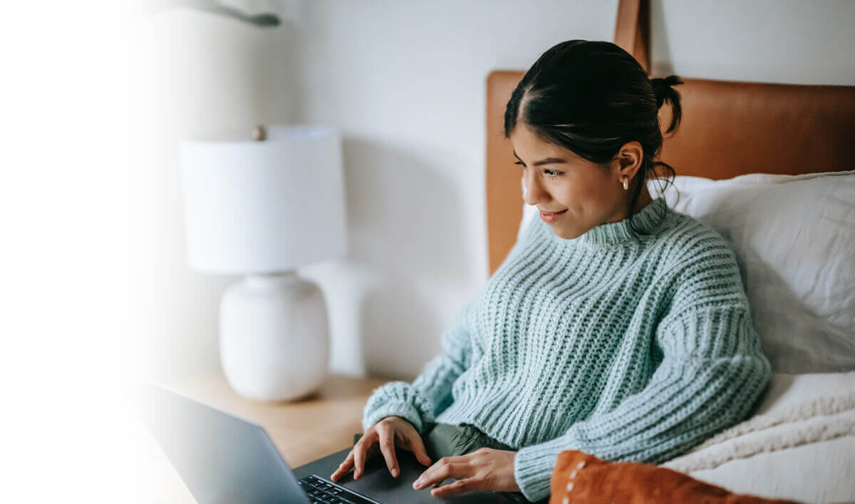 Frau sitzt vor dem Laptop im Bett